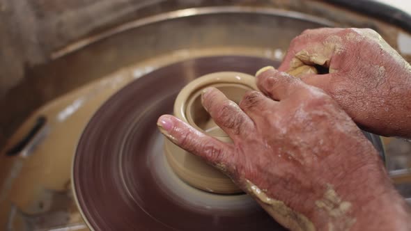 Male Hands of Potter Press Down Piece of Clay Spinning on Potter's Wheel to Give It Different Shape