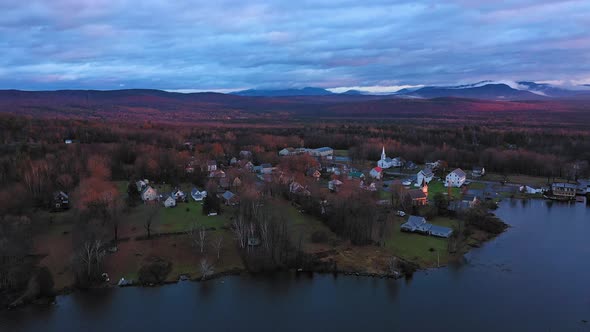 Aerial footage flying over lake at sunrise in late fall towards small rural community with misty mou