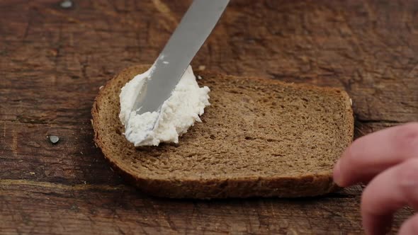 hand with a knife spreads white cottage cheese 