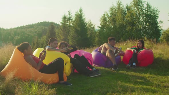 Positive Diverse Multiracial Travelers Enjoying Leisure on Air Couches on Mountain Top at Daybreak