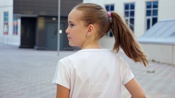 Blonde Teenage Girl on Pavement Against Large City Building