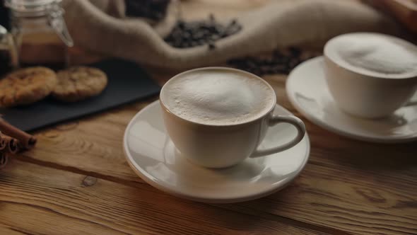 A Woman's Hand Takes One of Two Cups of Coffee Off the Table