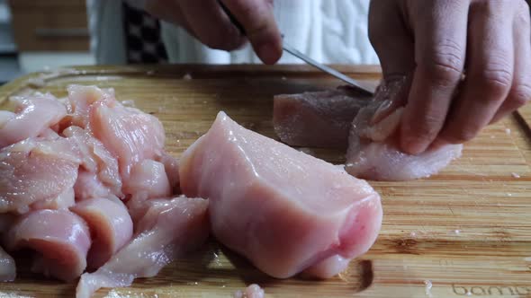 Hands Cutting Fresh Chicken Meat Fillet On Wooden Chopping Board In The Kitchen - close up