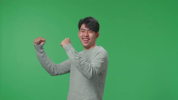 Side View Of Happy Asian Man Celebrating While Standing In Front Of Green Screen Background