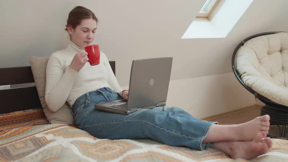 Young girl works remotely from home on bed at the computer.