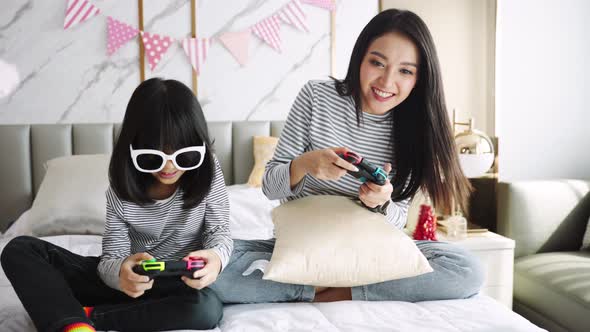 Asian young mother and young child are playing video game on couch at home,