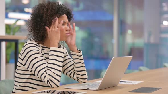 African Woman with Laptop Having Headache in Office