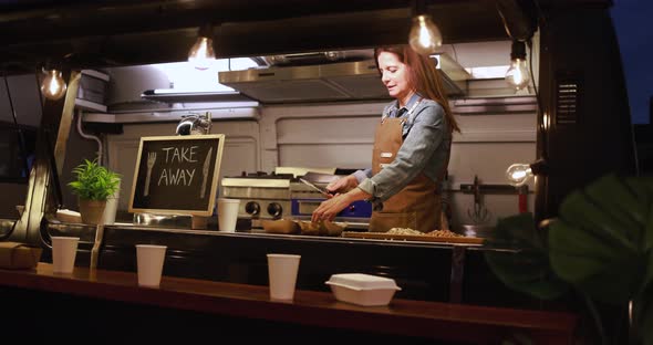 Caucasian chef woman working inside food truck at night time preparing dinner food