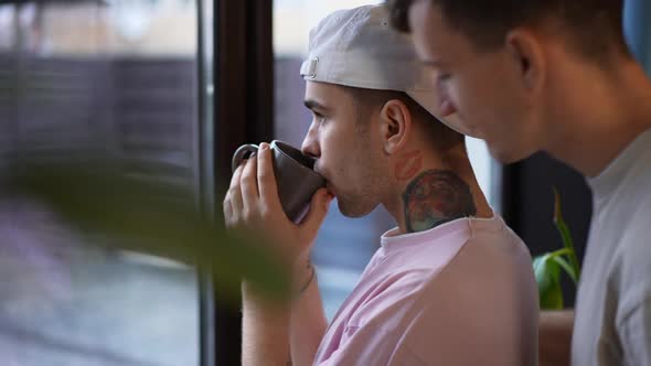 Closeup Portrait of Thoughtful Young Gay Man Looking Out Window Drinking Morning Coffee As Boyfriend