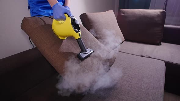 Furniture and Apartment Cleaning Concept. Man Cleaning Couch with Steam Cleaner at Home