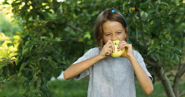 Cute little girl eat green apple in home garden outdoor, happy child