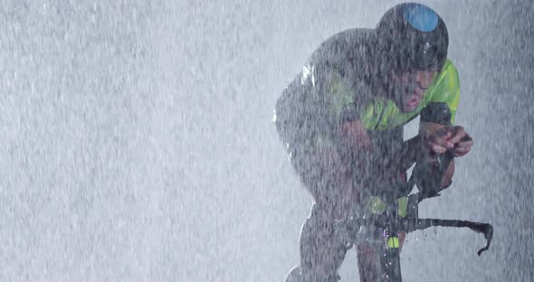 Triathlon Athlete Riding a Professional Racing Bicycle on an Intense Workout in Dark with Rain