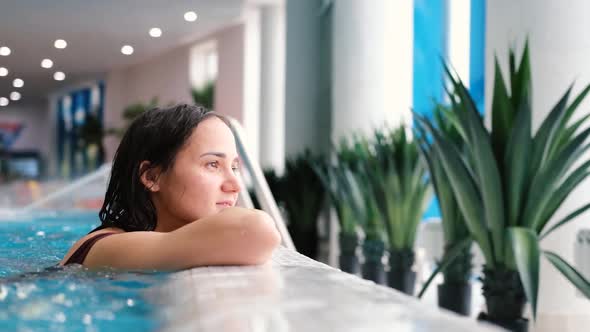 Beautiful Young Woman Relaxes in the Pool Looking Into the Large Light Window Into the Distance