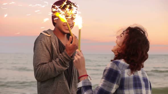 Cheerful Smiling Multiethnic Couple Holding Burning Sparkling Candles Standing By the Sea During