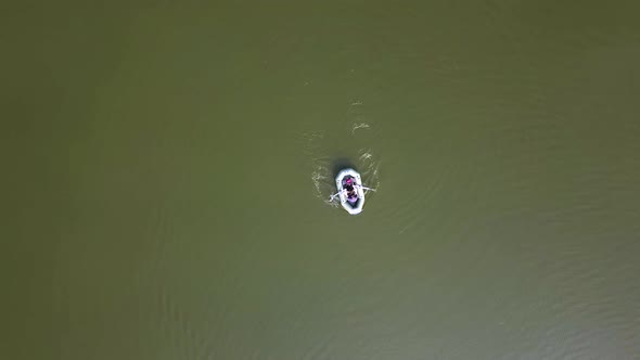 Aerial view of young man swimming on inflatable rafting rubber boat on lake water surface.