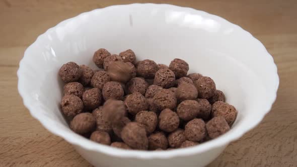 Crispy cereal chocolate flakes balls fall into a white bowl