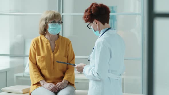 Doctor in Mask Measuring Temperature of Elderly Woman in Clinic