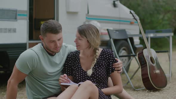 Lovely couple sitting together and reading a book against motor home RV campervan