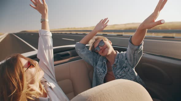 Two Beautiful Young Women Ride in White Convertible Driving on Highway Against Background of Field