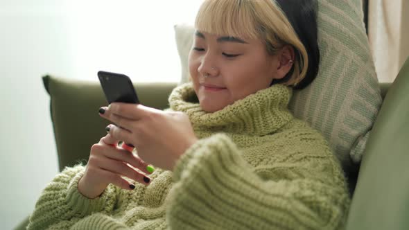 Positive Asian woman typing by phone