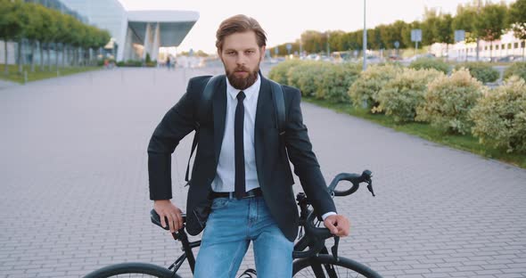 Stylish Man with Beard Which Sitting on His Bike on Pedestrian Path Near Big Urban Construction