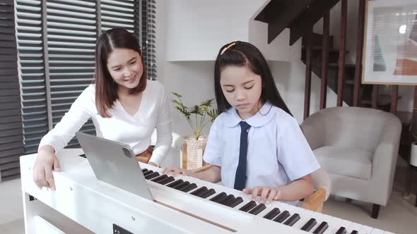 Mother accompanying daughter during virtual piano lessons.