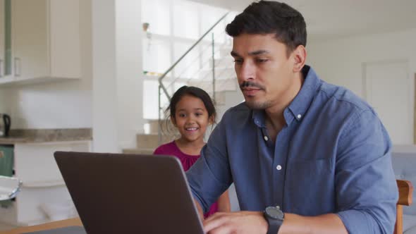 Happy hispanic father and daughter sitting at table looking at laptop