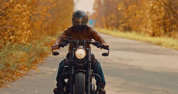 Male Biker in Glasses and a Helmet Rides a Cool Motorcycle in the Fall Along the Highway