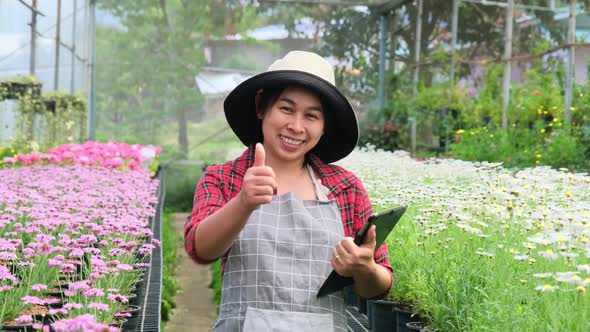 Beautiful gardener woman uses a tablet while working in a greenhouse.