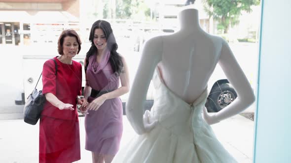 Mother and daughter looking at wedding dress in shop window