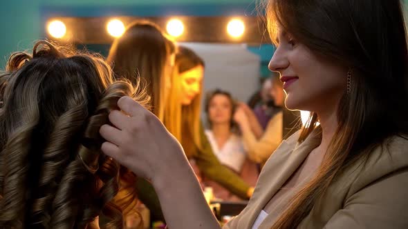 Hairdresser Doing Curly Hairstyle to Young Blonde Woman in Beauty Salon