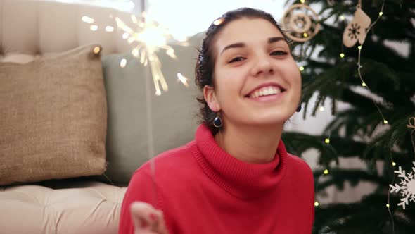 Happy Attractive Young Woman Sitting on the Floor By the Christmas Tree Celebrating Xmas with