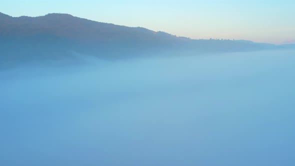 4K aerial view over mountain at sunrise in heavy fog. golden morning sunlight