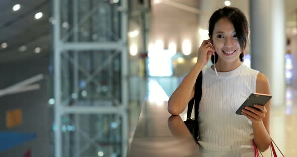 Woman using smart phone and holding paper bags in shopping mall 