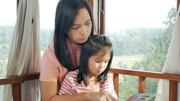 Closeup of mother and daughter reading a book on the bed.