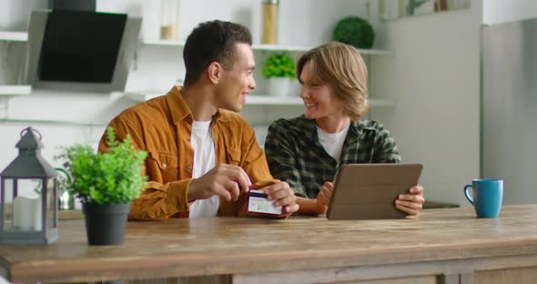 Cheerful Mixed Couple Are Doing Online Shopping in Kitchen