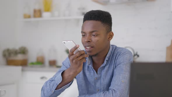 Confident African American Businessman Recording Voice Mail on Smartphone Sitting in Kitchen at Home