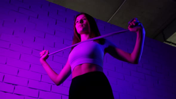 Young Woman Doing Pilates Exercises  Working Out Her Hands Using an Elastic Band in Neon Lighting