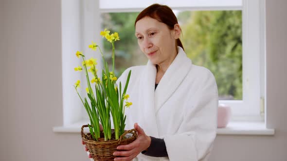 Positive Mature Caucasian Woman Admiring Yellow Flowers in Wicker Basket Looking at Camera