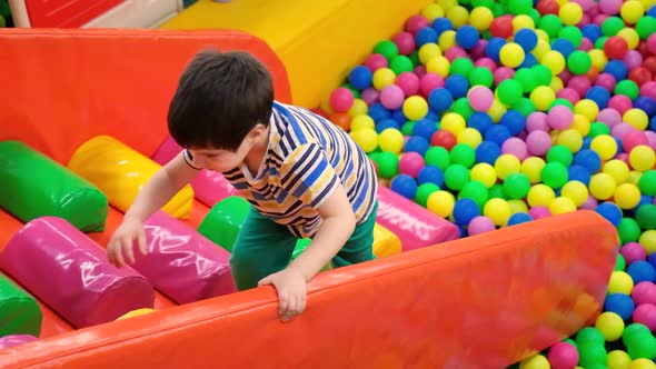 The Boy Climbs the Slide on a Colored Soft Staircase From the Pool with Soft Balls