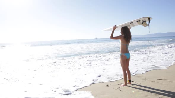 A young woman surfer walking out into the ocean while holding surfboard above head.