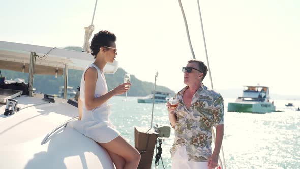 4K Caucasian couple drinking champagne together while catamaran boat sailing at summer sunset.
