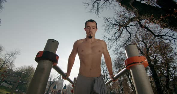 Young Man Is Doing Push-ups on Bars with Clapping His Arms in Good Weather 