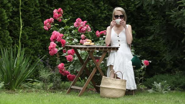 Blonde girl drink a coffee in garden with roses on background