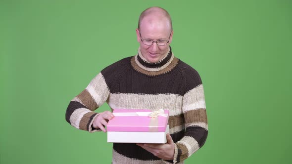 Happy Mature Bald Man Looking Surprised While Opening Gift Box