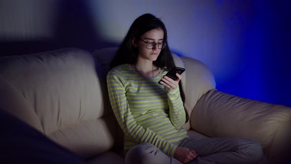 Late at night, a young brunette is sitting at the TV with a phone in her hands, camera movement