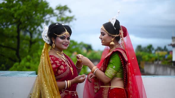 Two cheerful Indian bengali brides laughing together and talking outdoor cloudy sky