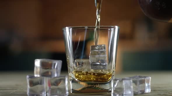 old single malt whiskey is poured from bottle into a clear glass with ice cubes.