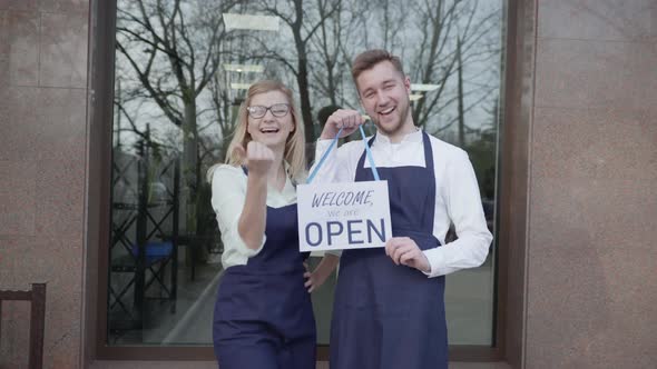 Open Shop, Young Partners Rejoice at Opening of Small Business, Standing with Sign Open