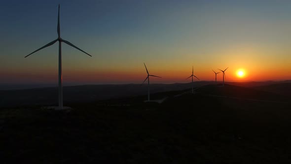 Sun setting behind elegant windmills on a hill alt